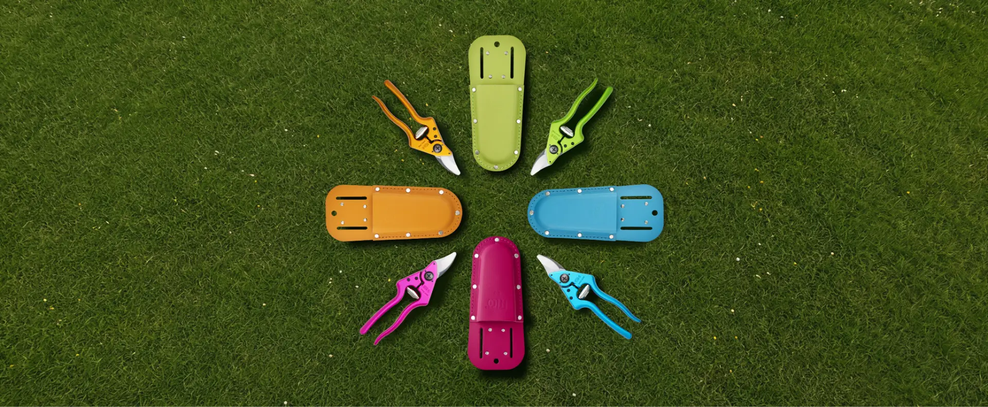 Four colorful FELCO pruning shears with matching holsters arranged on grass